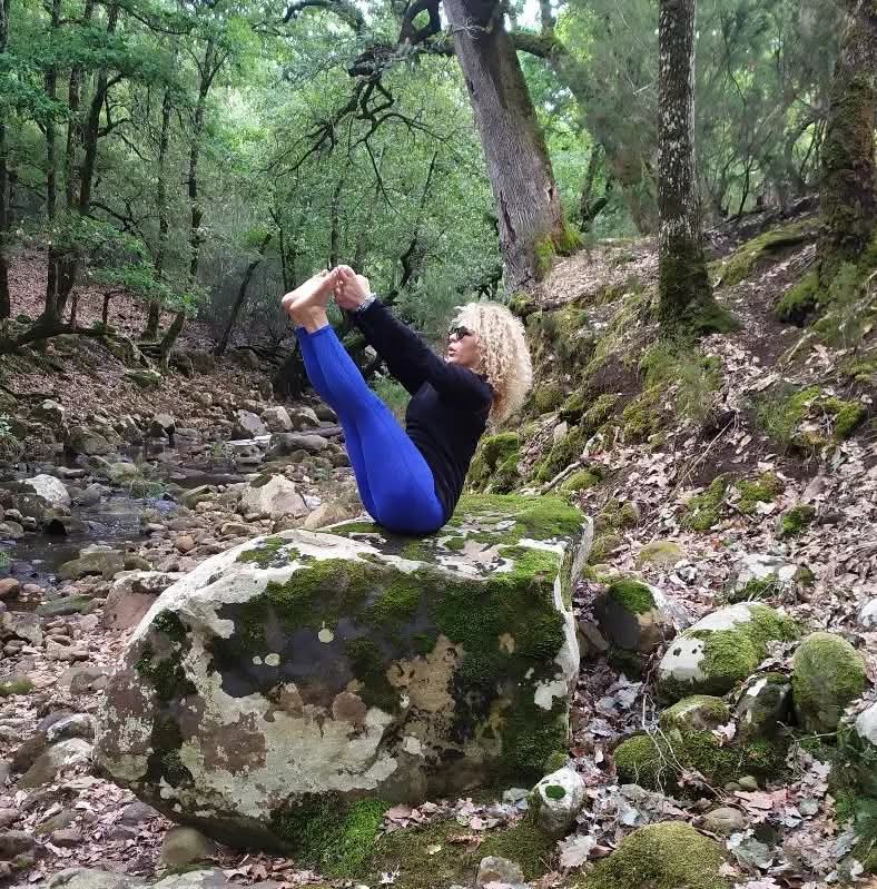 Sinda Flora practicing a strong boat pose beside a wooded stream