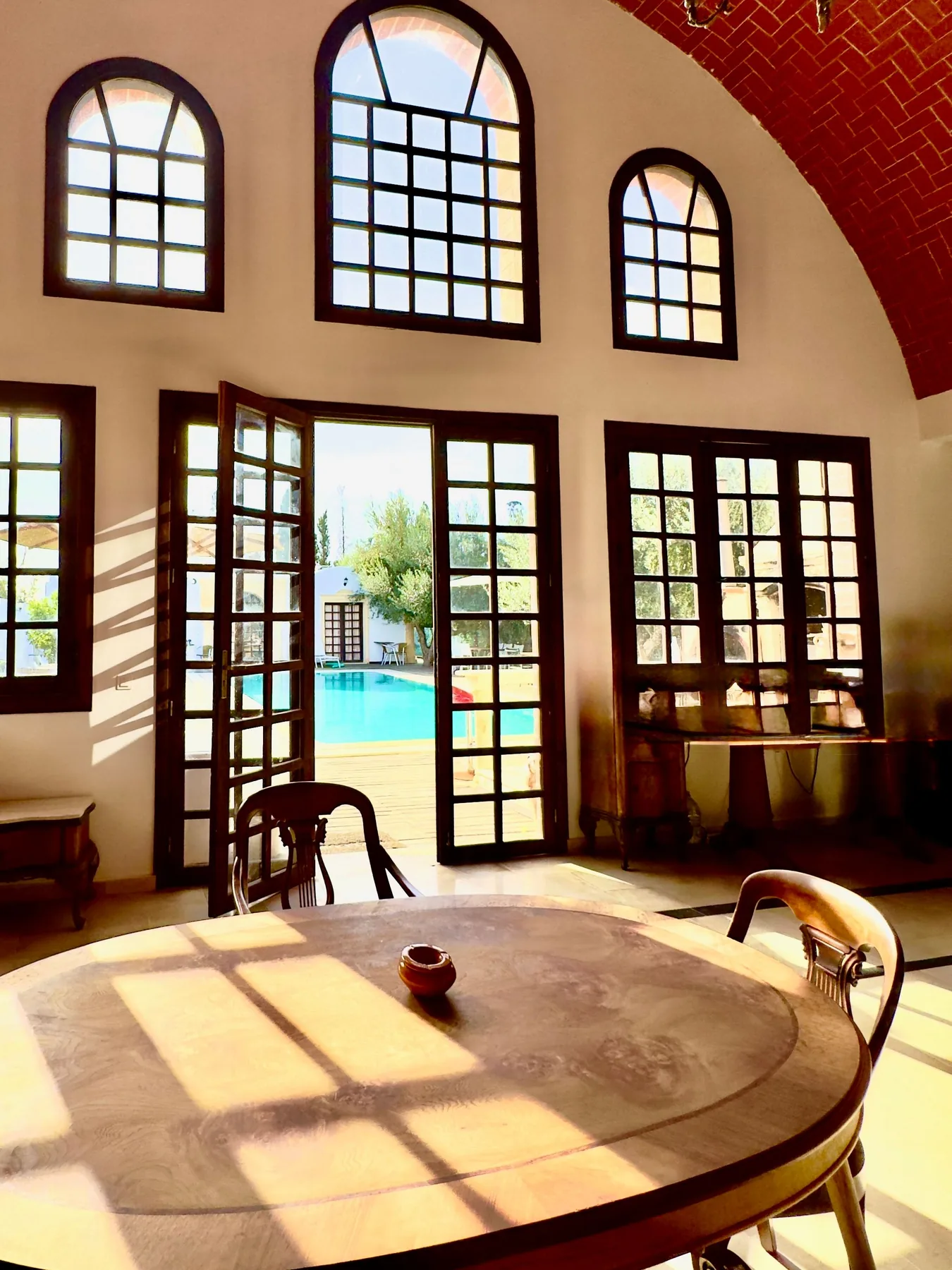 Sunlit table beside tall arched windows overlooking the pool at the Trinity Soul retreat property